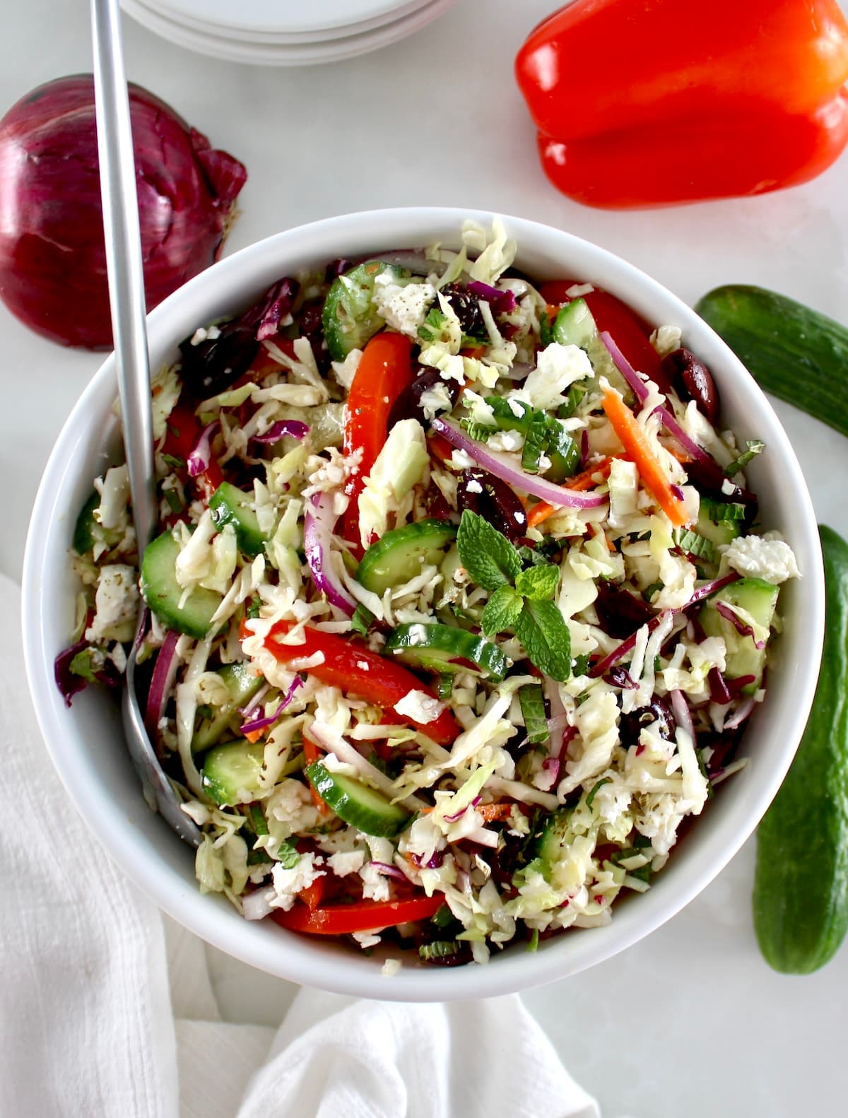 overhead view of Greek Coleslaw in white bowl with silver serving spoon on side