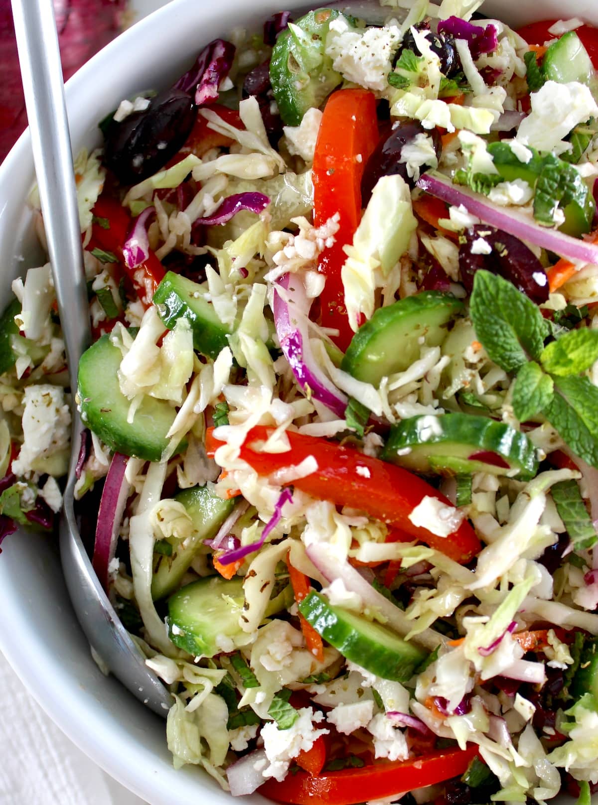 closeup of Greek Coleslaw in white bowl with serving spoon on side
