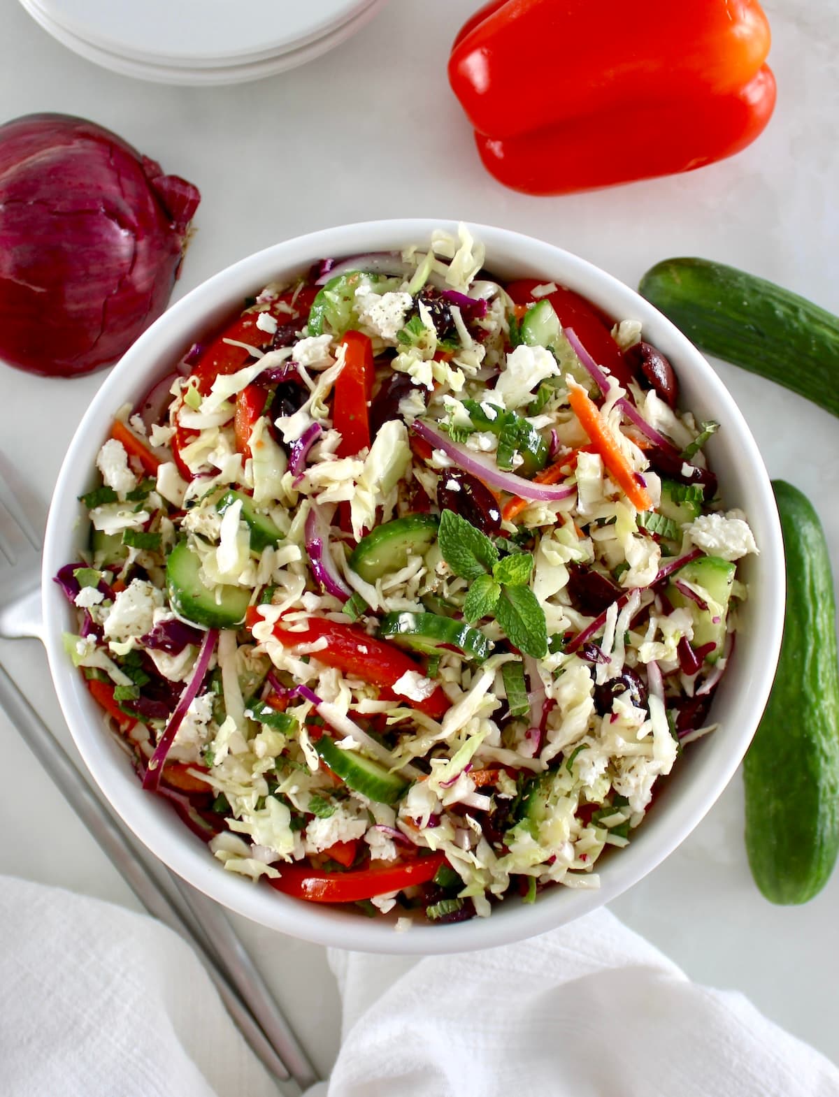 overhead view of Greek Coleslaw in white bowl with veggies around