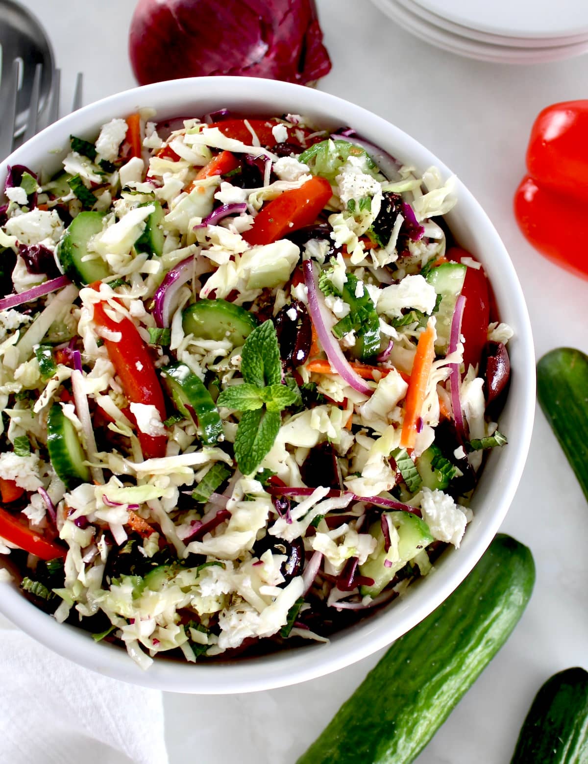 overhead view of Greek Coleslaw in white bowl with fresh veggies around