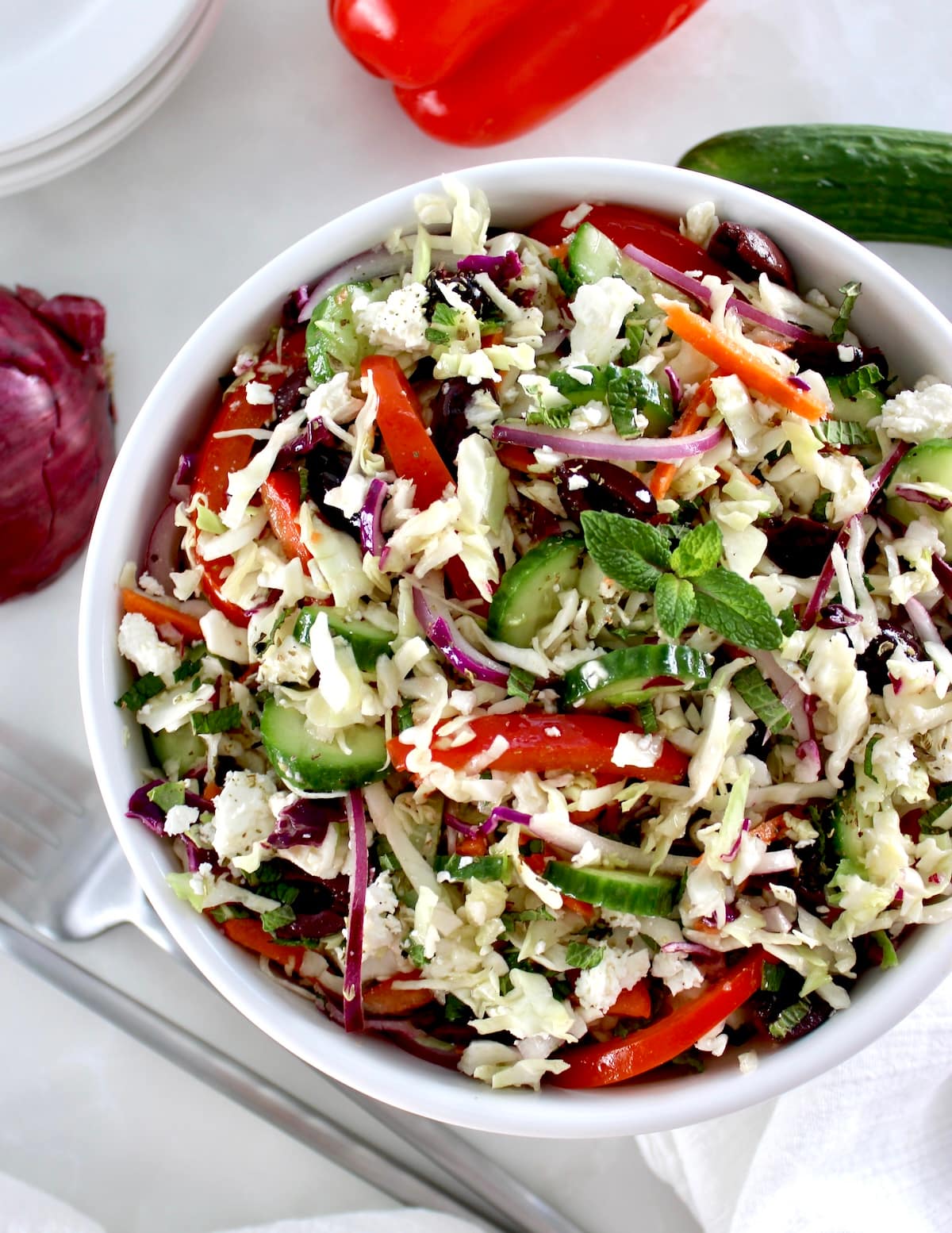 overhead view of Greek Coleslaw in white bowl with fresh veggies around