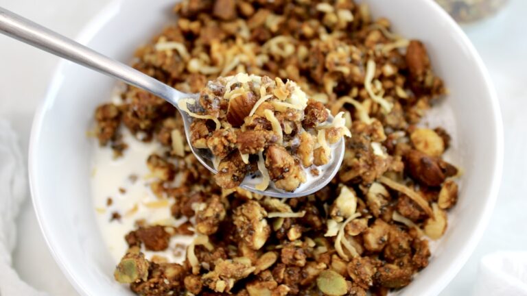 Keto Granola held up with spoon over bowl with milk