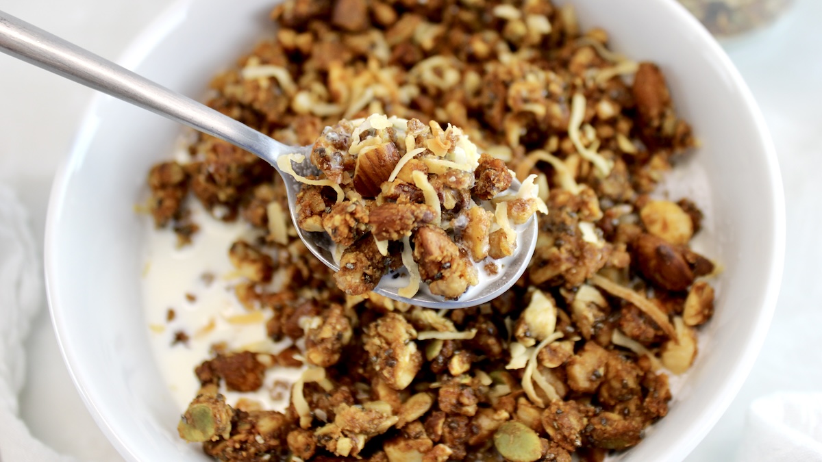 spoonful of Keto Granola held up over bowl with milk