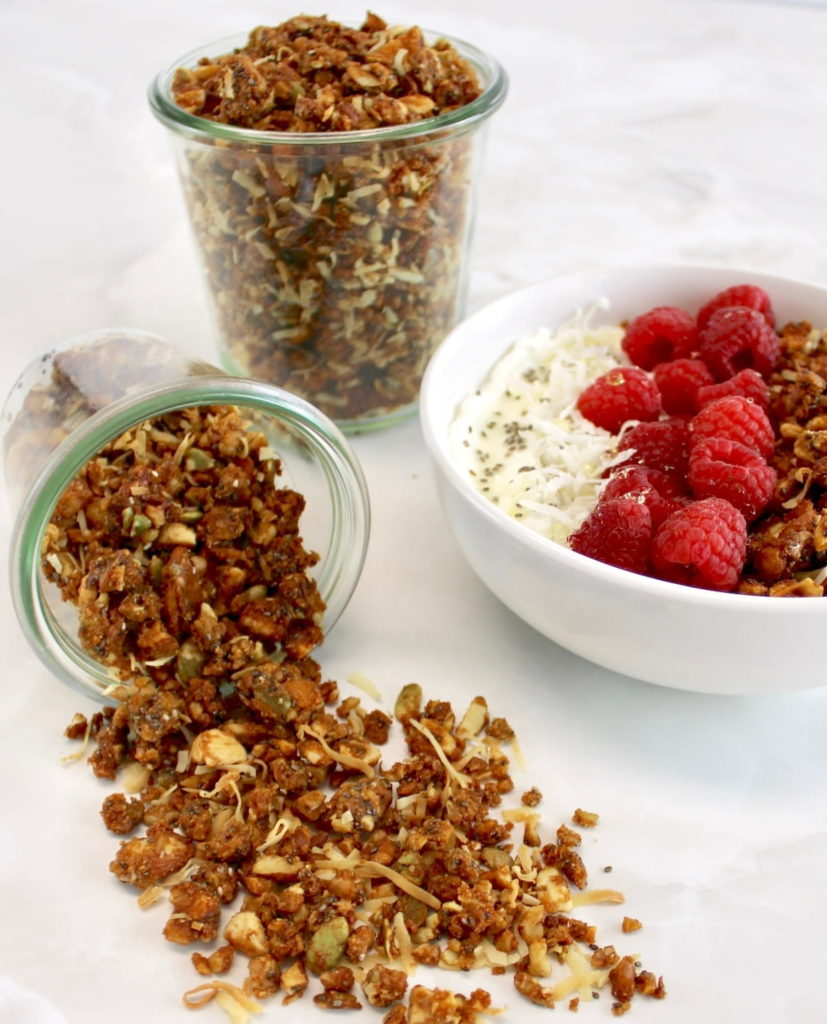Keto Granola spilling out of jar with raspberry yogurt bowl in back