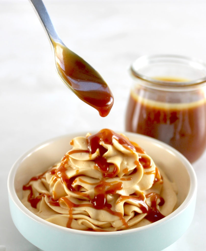 Keto Salted Caramel Cheesecake Mousse in blue bowl with caramel dripping off spoon over it