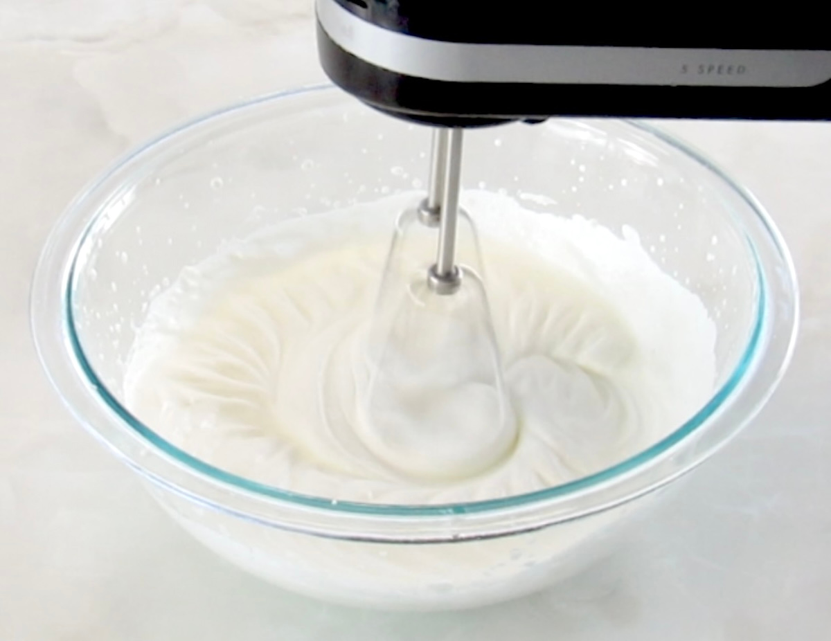 heavy cream being whipped in glass bowl with hand mixer