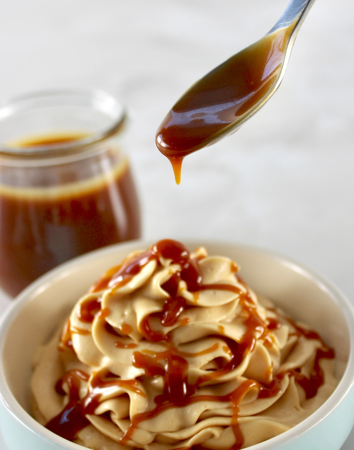 caramel being spooned over Keto Salted Caramel Cheesecake Mousse in blue bowl