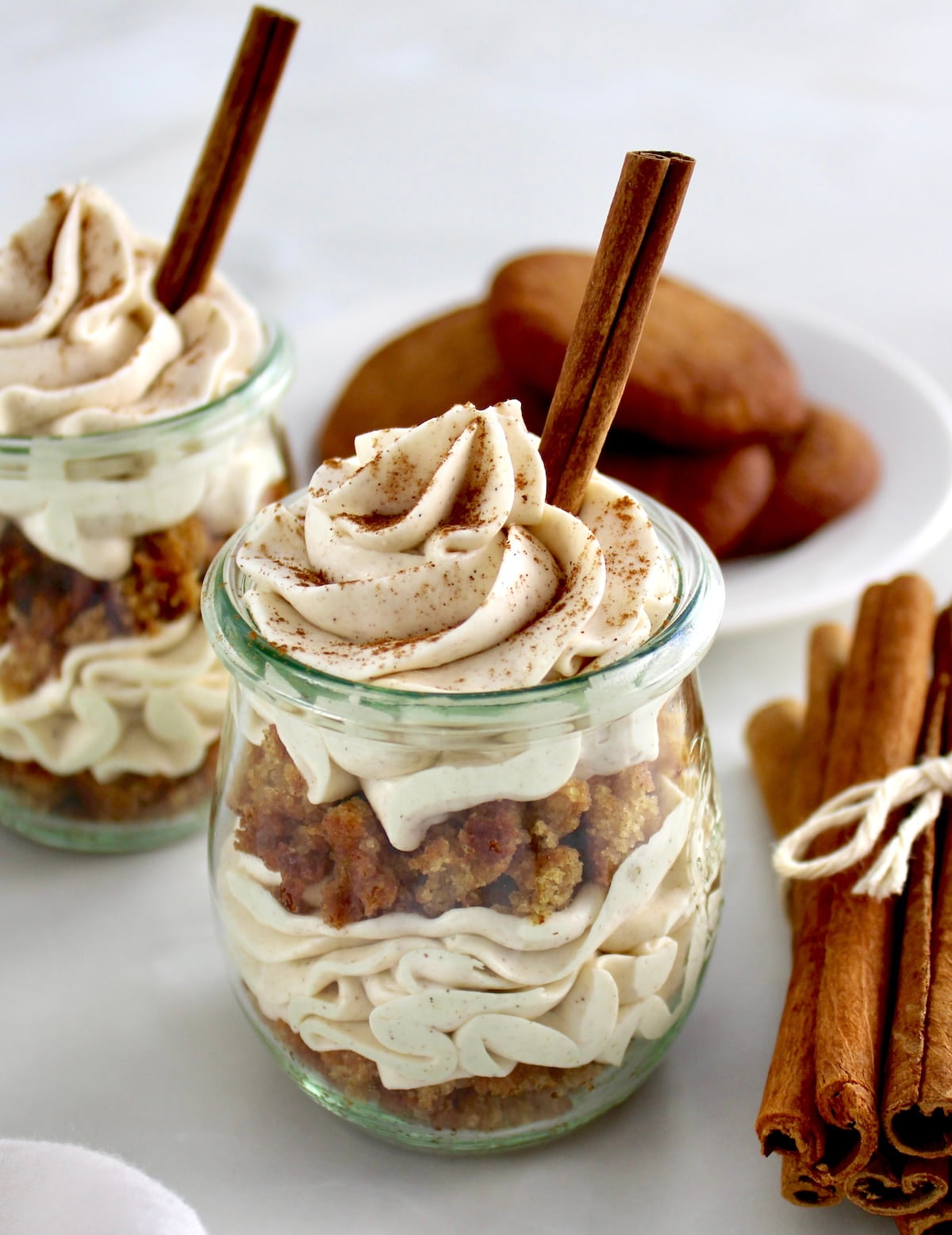 Keto Snickerdoodle Cheesecake Parfaits in open glass jars with cinnamon stick on top and on side