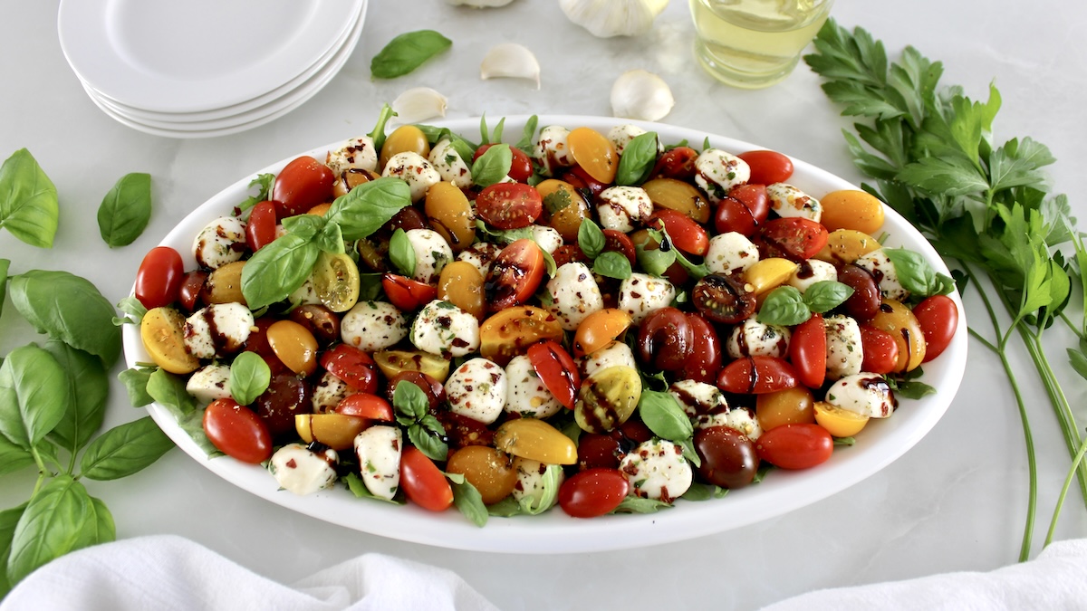 Chopped Caprese Salad on white oval platter with fresh basil leaves