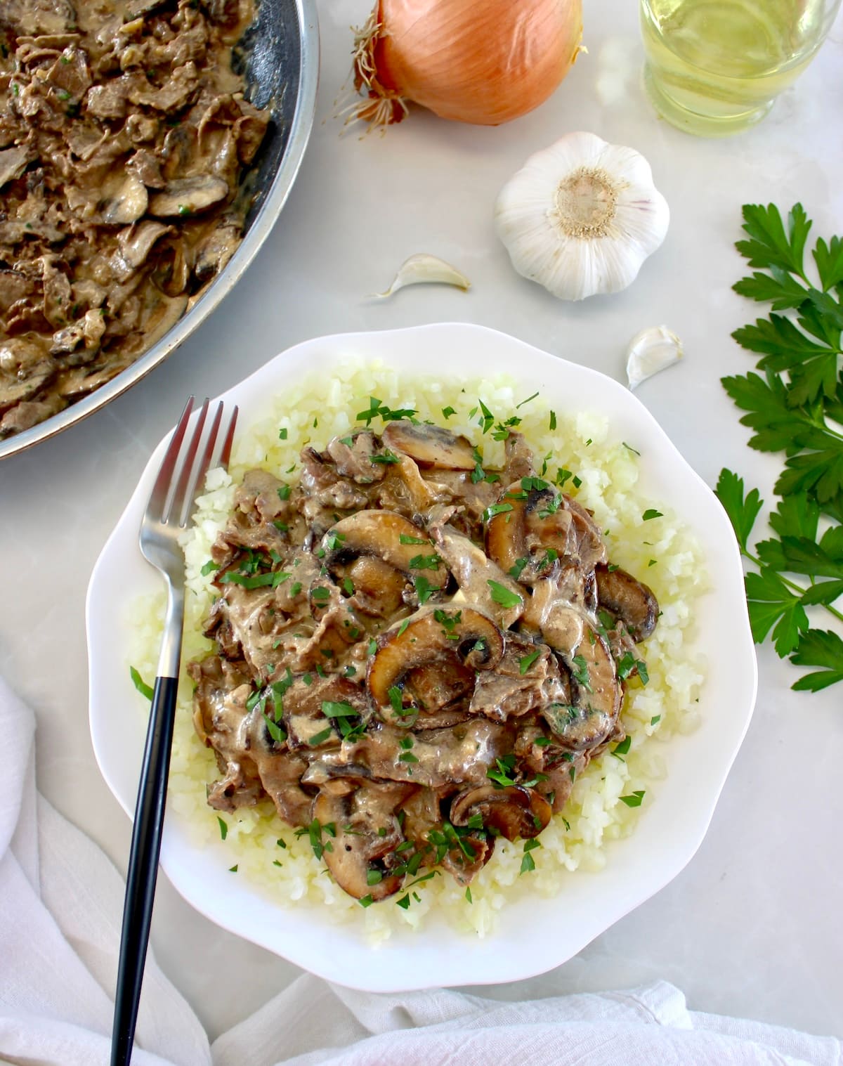 Easy Beef Stroganoff over cauliflower rice in white bowl with skillet in back