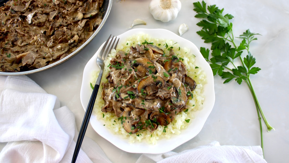 Easy Beef Stroganoff over cauliflower rice in white bowl with skillet in back
