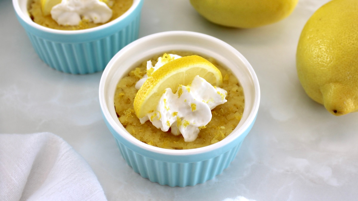Keto Lemon Mug Cake in blue ramekin with whip cream and lemon slice on top
