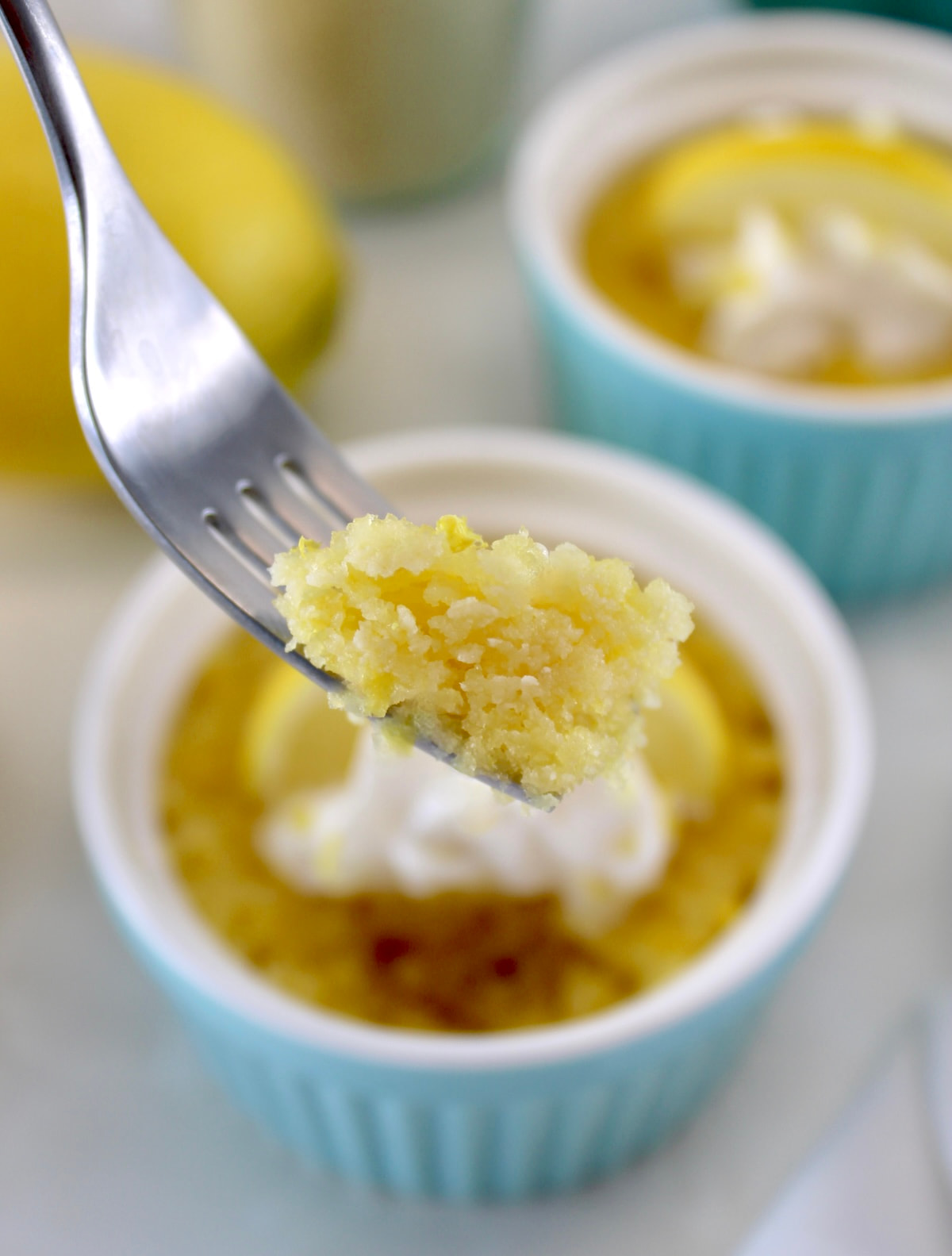 fork holding up piece of Keto Lemon Mug Cake over blue ramekin