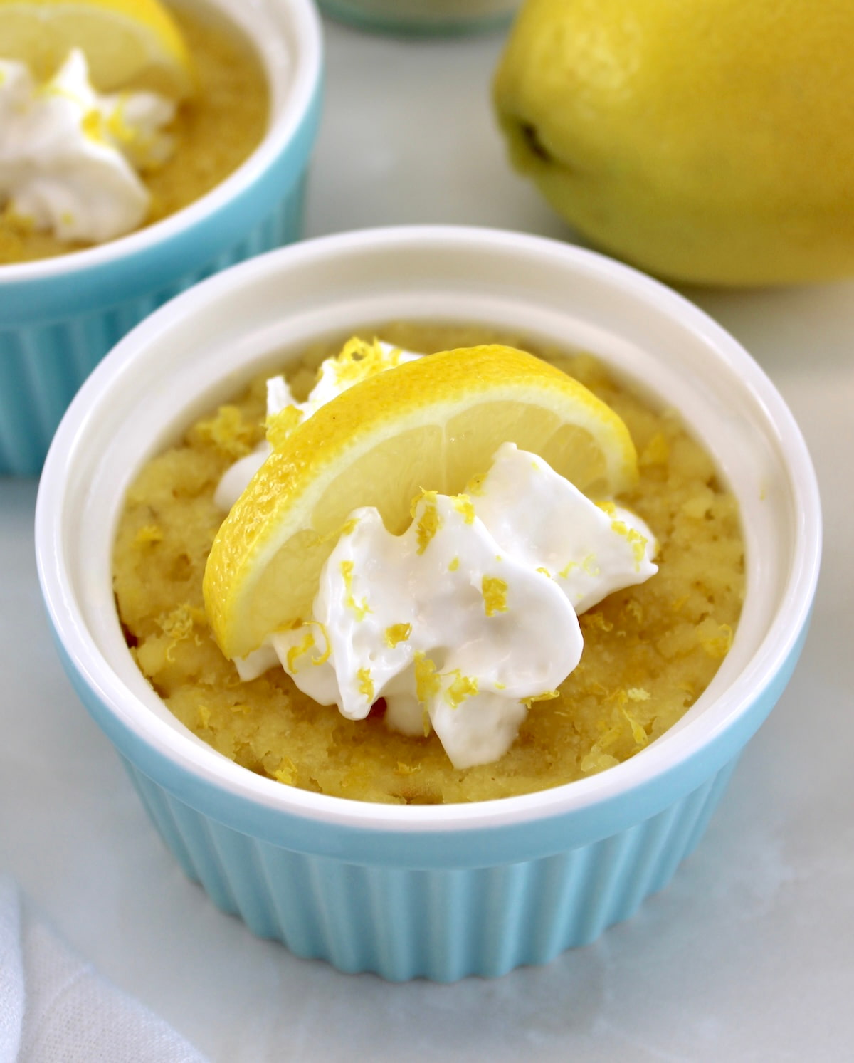 closeup of Keto Lemon Mug Cake in blue ramekin with whip cream and lemon slice on top