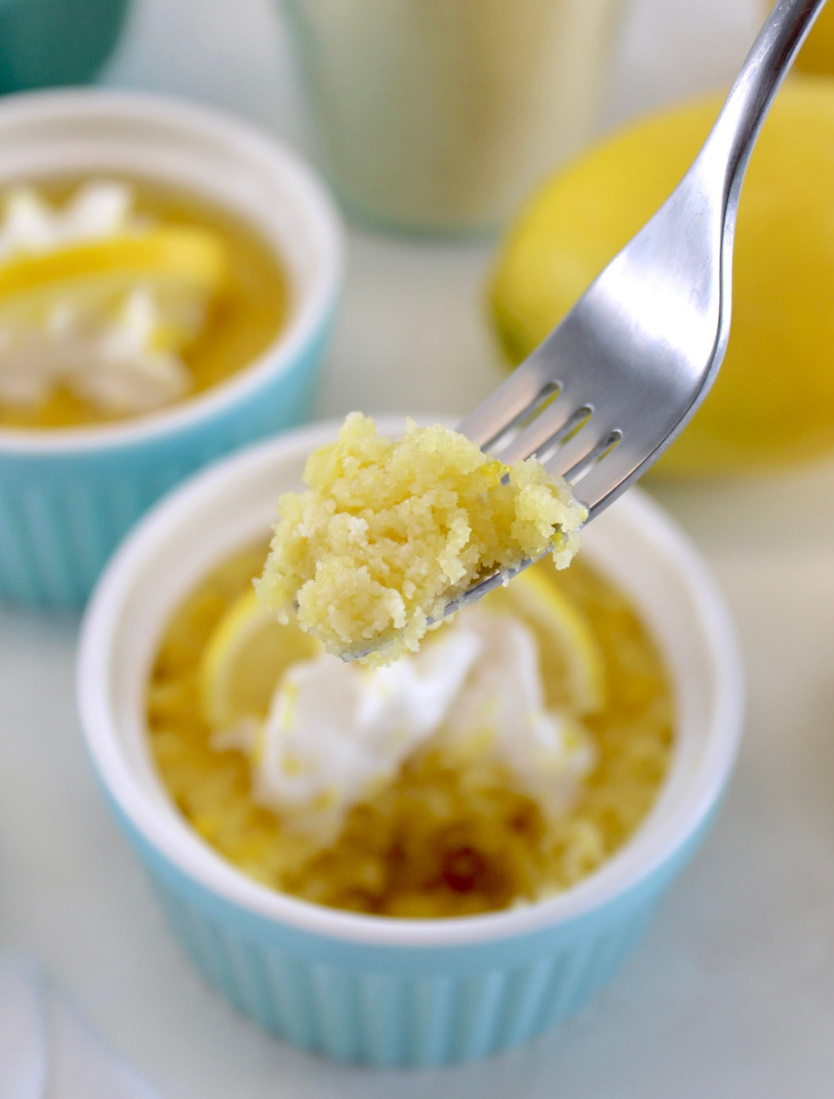 fork holding up piece of Keto Lemon Mug Cake over blue ramekin