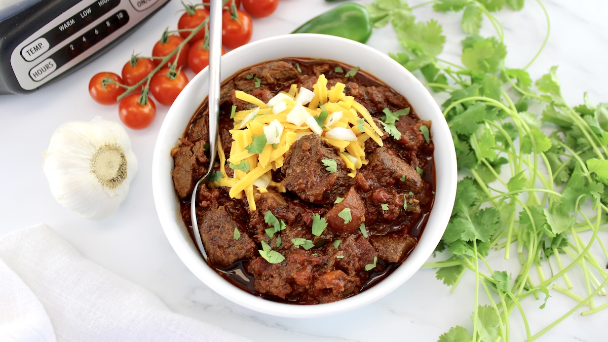 overhead view of Slow Cooker Texas Chili in white bowl with spoon and cheese on top