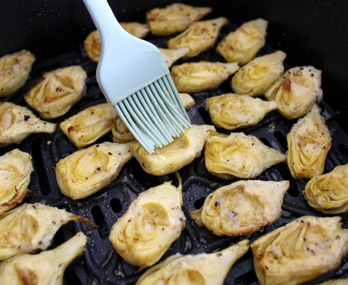 artichoke hearts in air fryer basket being brushed with garlic butter