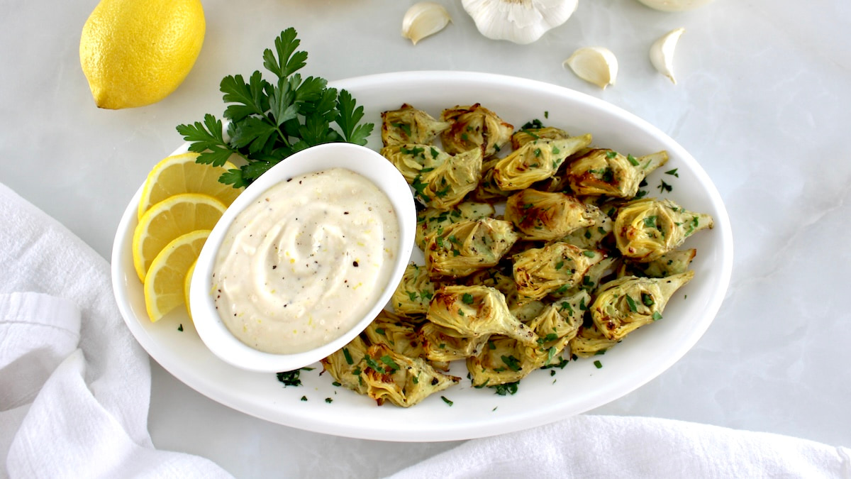 Air Fryer Artichoke Hearts on white oval platter with lemon slices and garlic aioli