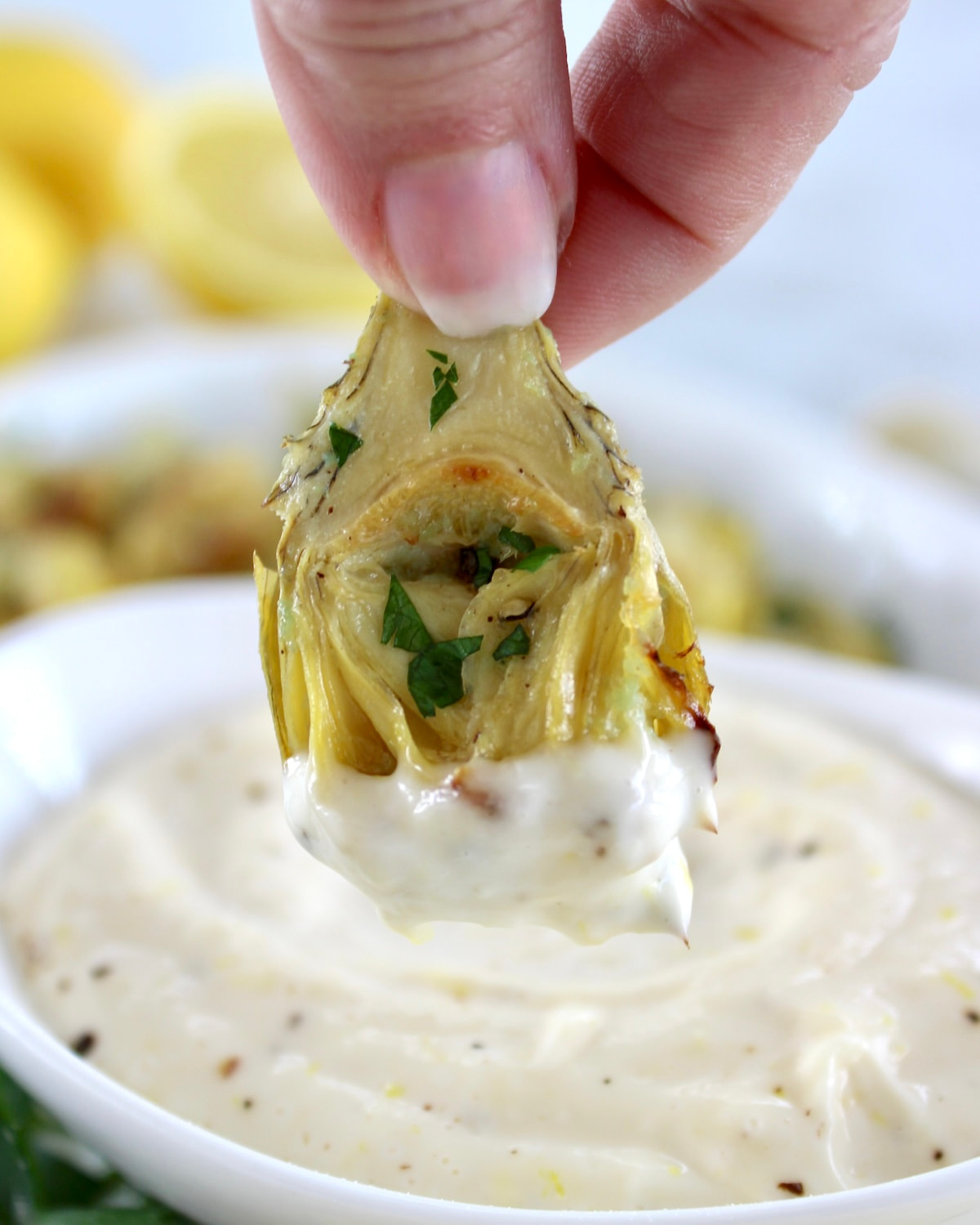 dipping Air Fryer Artichoke Heart in garlic aioli in white bowl