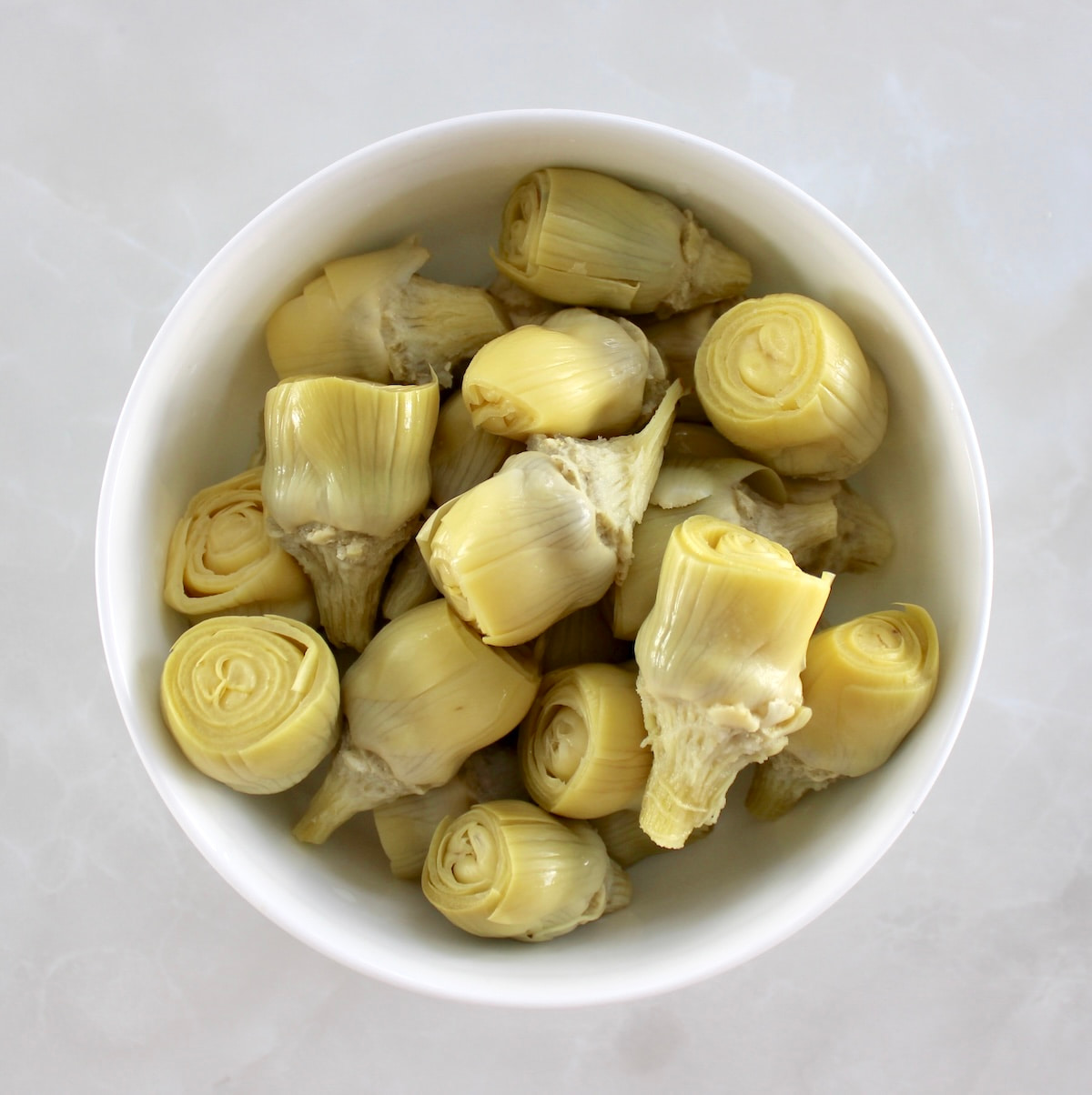 overhead view of whole artichoke hearts in white bowl
