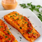 Bang Bang Salmon on white plate with sauce in back in open glass jar