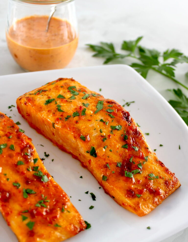 Bang Bang Salmon on white plate with sauce in back in open glass jar
