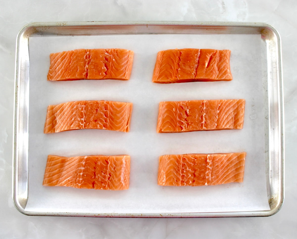 6 pieces of raw salmon on parchment lined baking sheet