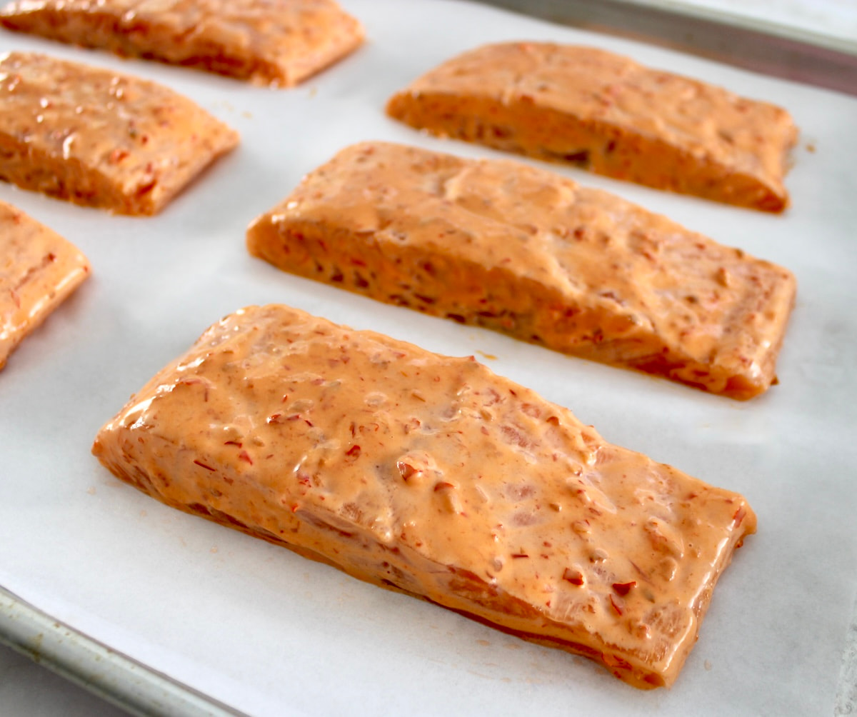 raw salmon with bang bang sauce over the tops on parchment lined baking sheet