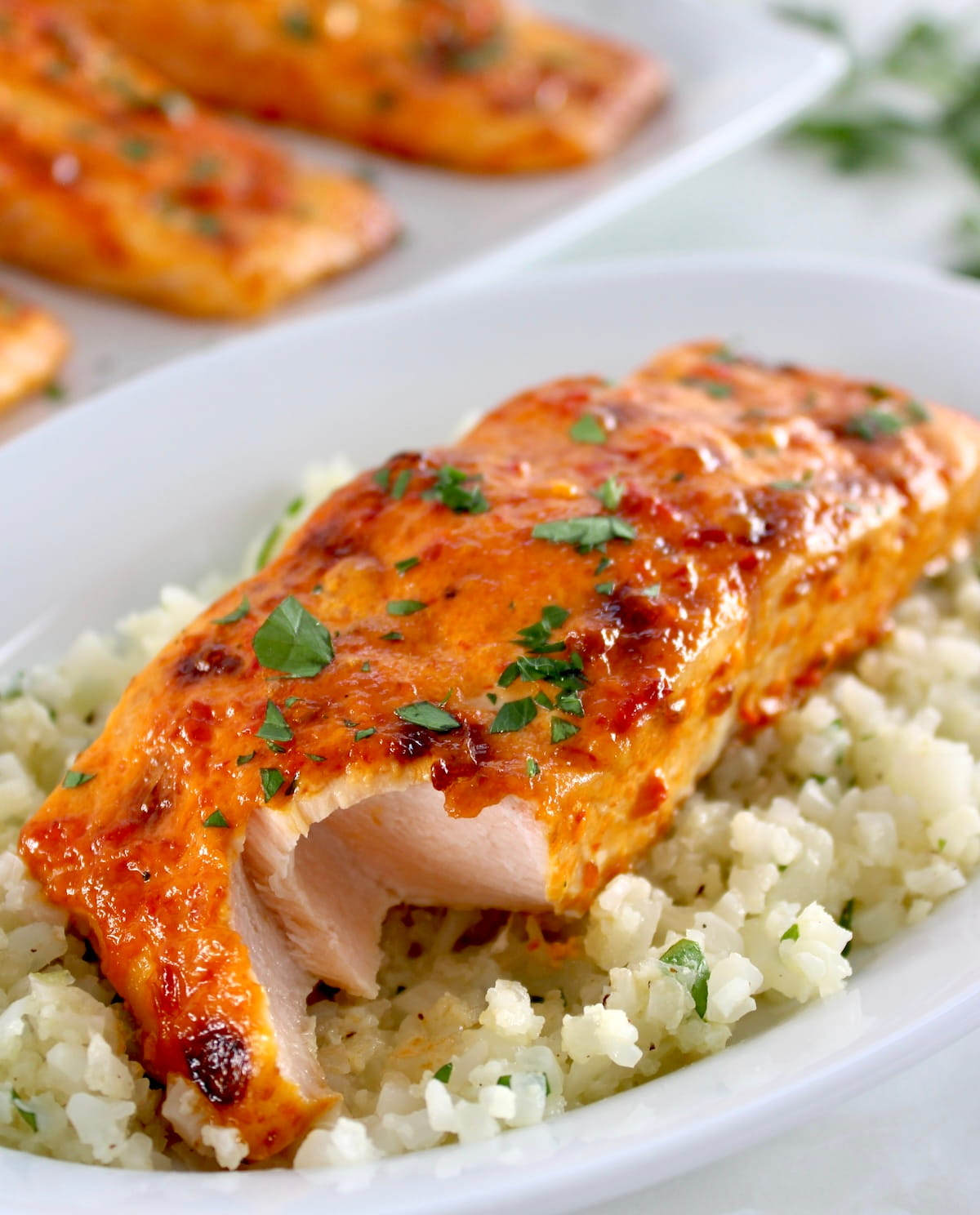 Bang Bang Salmon over cauliflower rice on white plate with bite missing