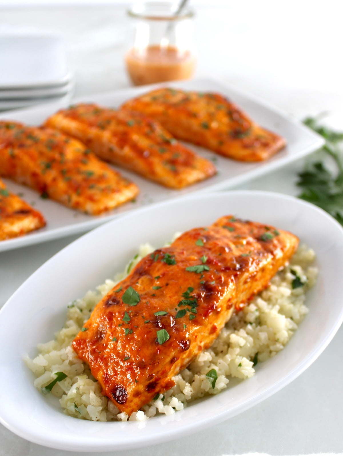 Bang Bang Salmon over cauliflower rice on white plate with more salmon on platter in back