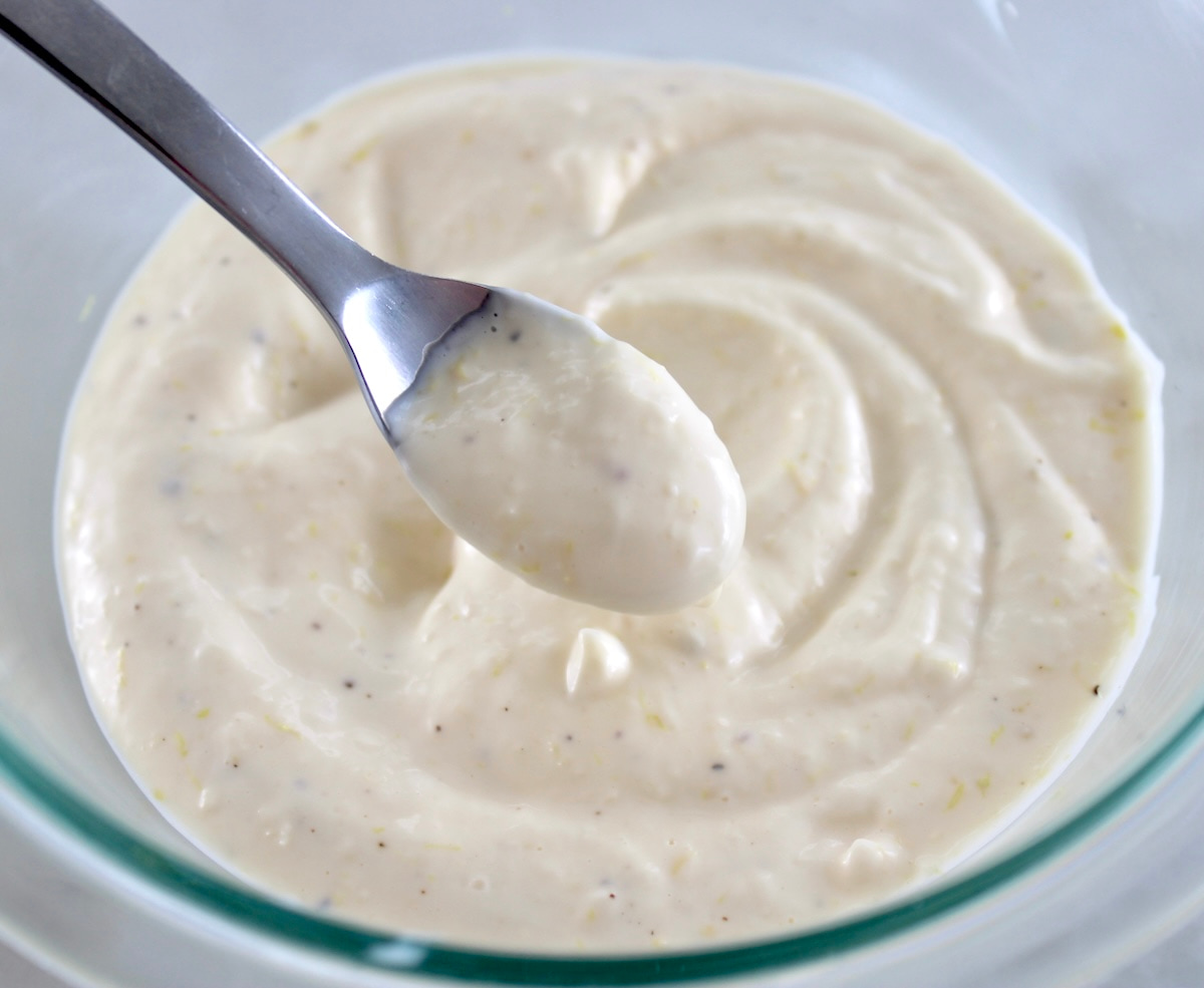 spoonful of Easy Garlic Aioli held up over glass bowl