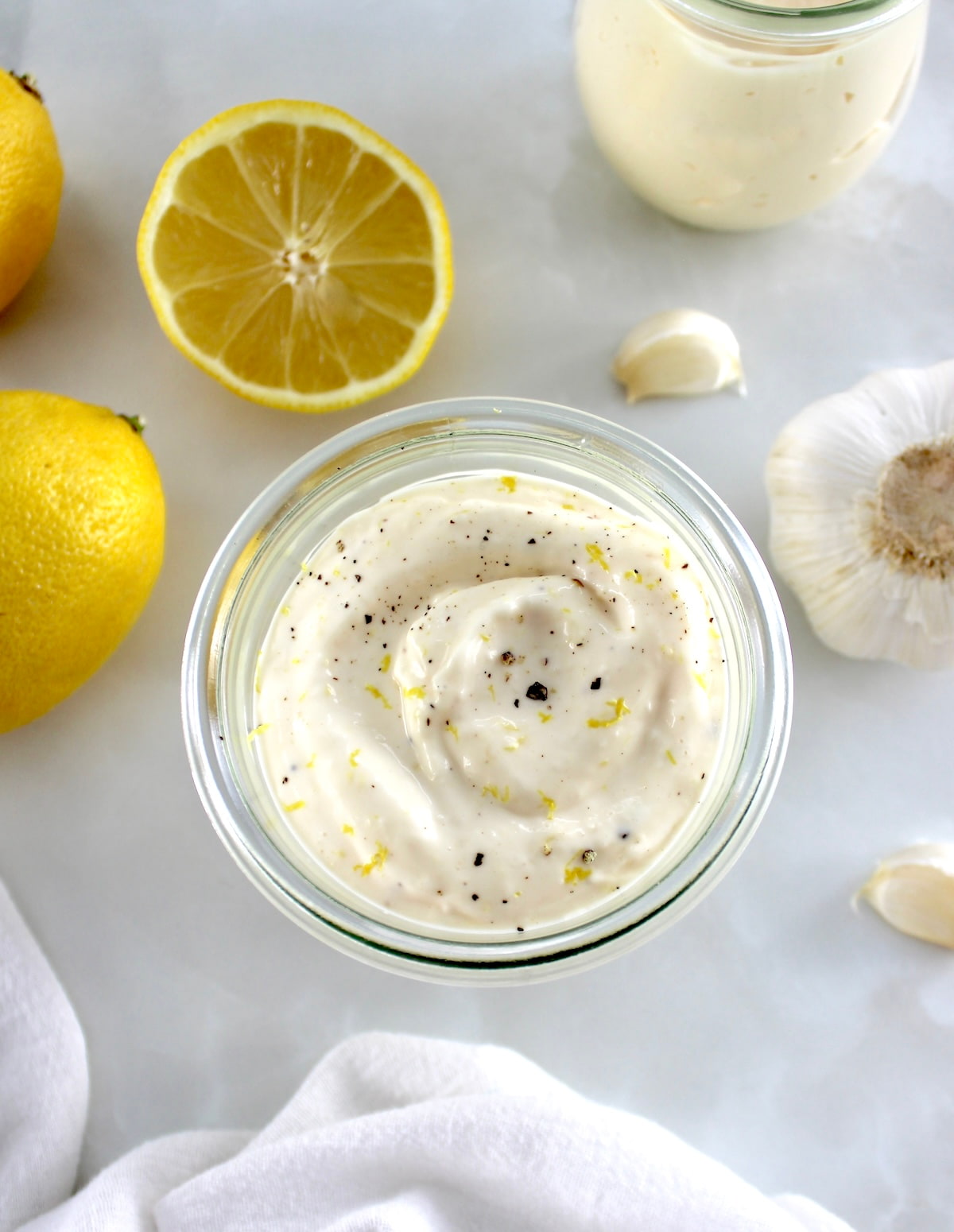 overhead view of Easy Garlic Aioli in open glass jar with lemons and garlic in back