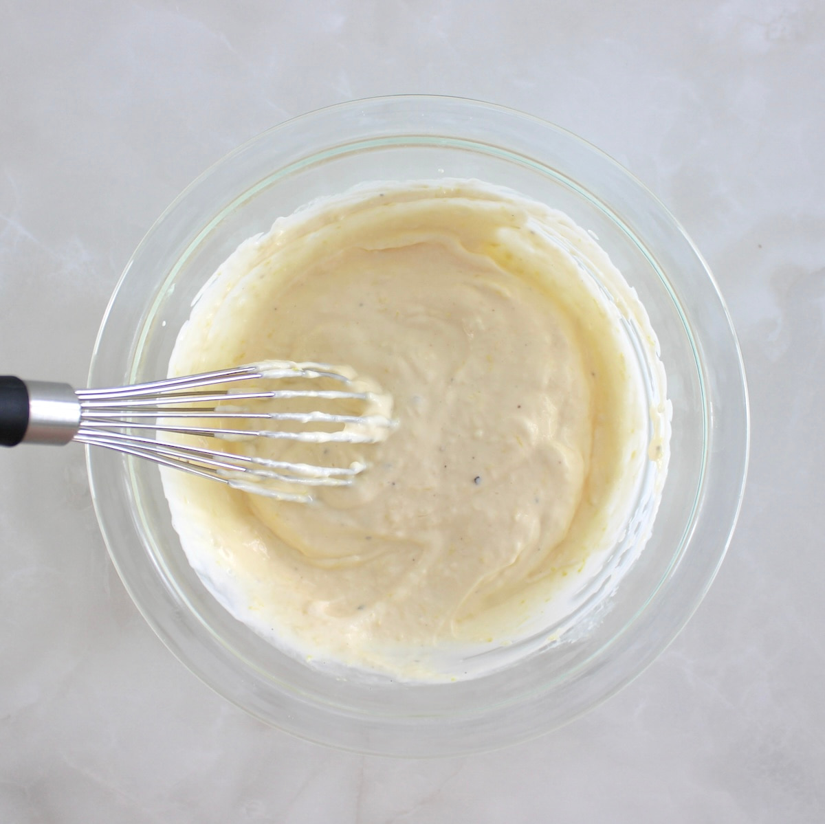 Easy Garlic Aioli in glass bowl with whisk