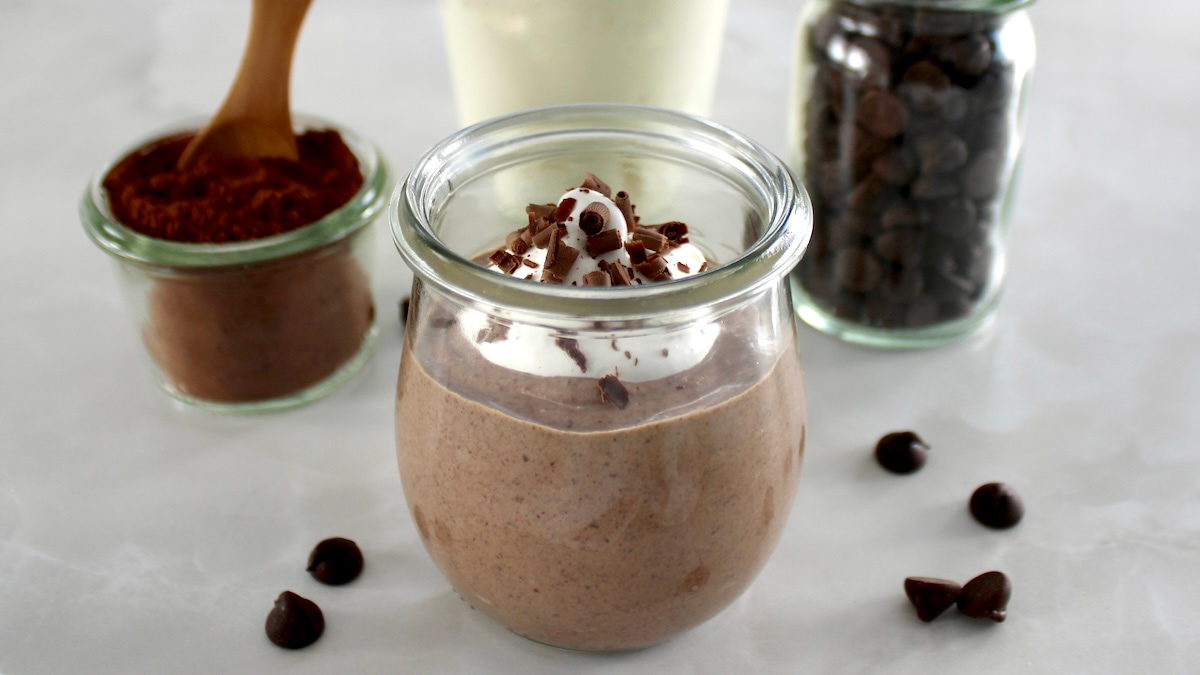 side view of Ricotta Chocolate Mousse in open glass jar with whip cream and shaved chocolate