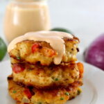 Shrimp Cakes stacked up on white plate with spicy mayo dripping from the top
