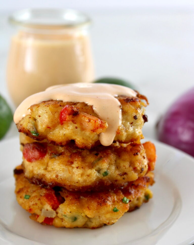 Shrimp Cakes stacked up on white plate with spicy mayo dripping from the top