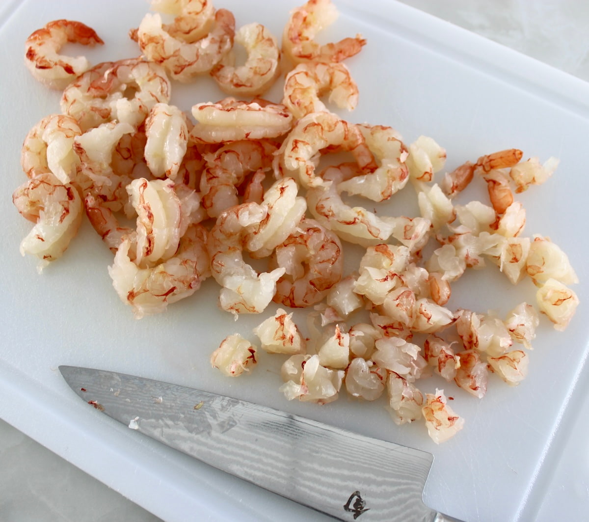 raw shrimp chopped on white cutting board with knife