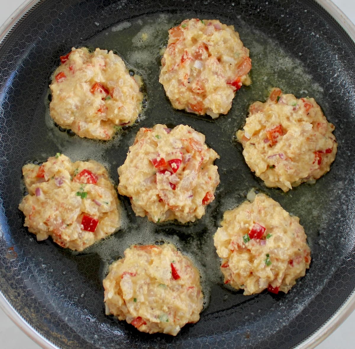 7 raw shrimp cakes frying in skillet