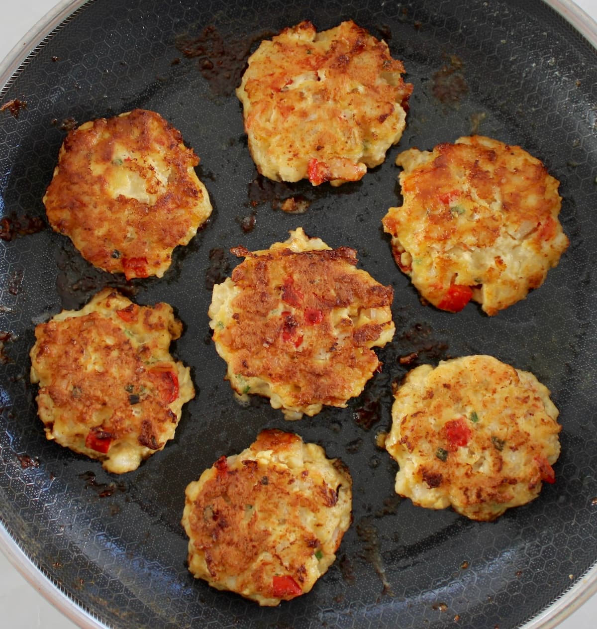 7 shrimp cakes frying in skillet