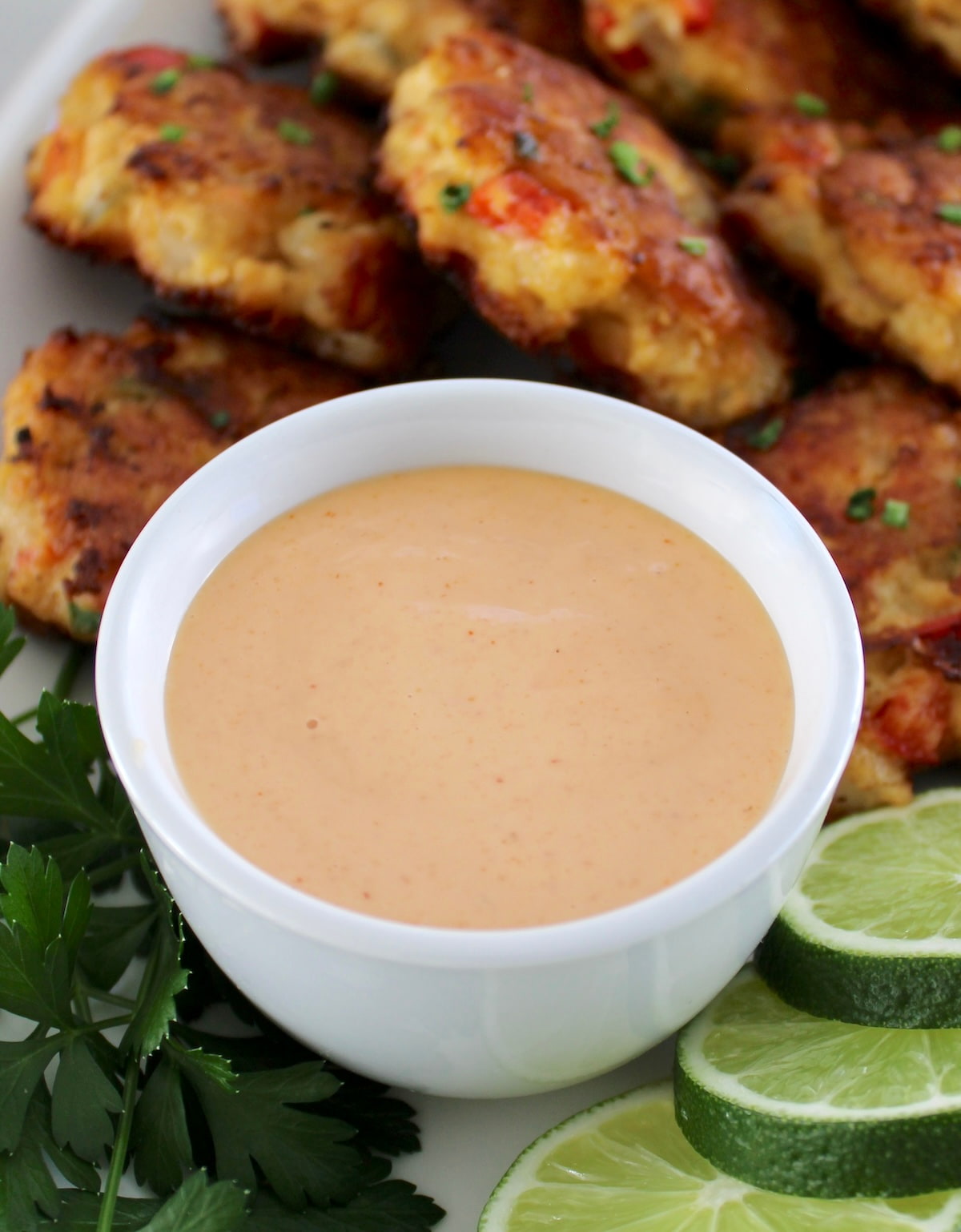 Spicy Mayo in white cup with patties and lime slices in back