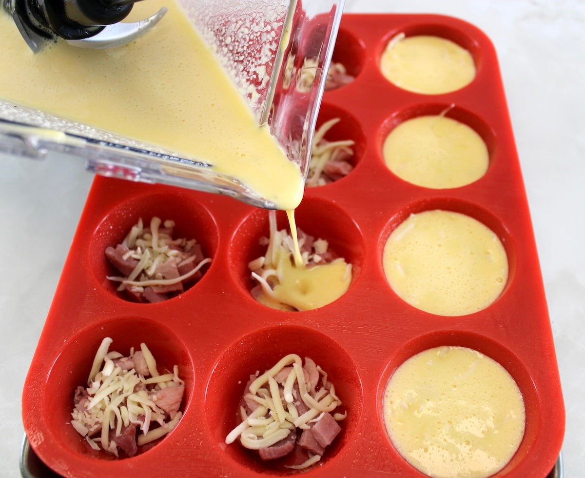 pouring Cottage Cheese  Egg Bites batter over chopped ham and cheese in red muffin pan
