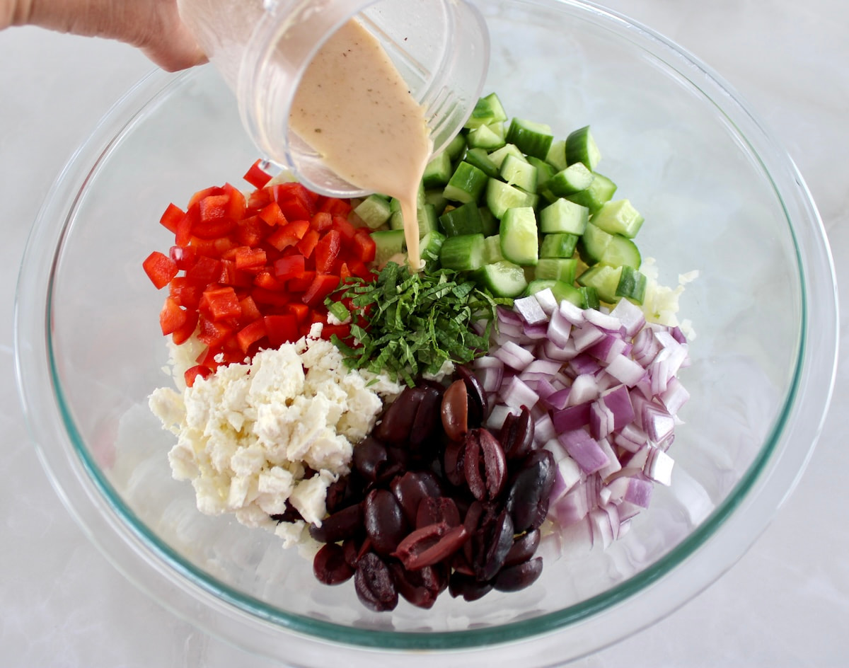 Greek Cauliflower Rice ingredients in sections in glass bowl with dressing being poured over top