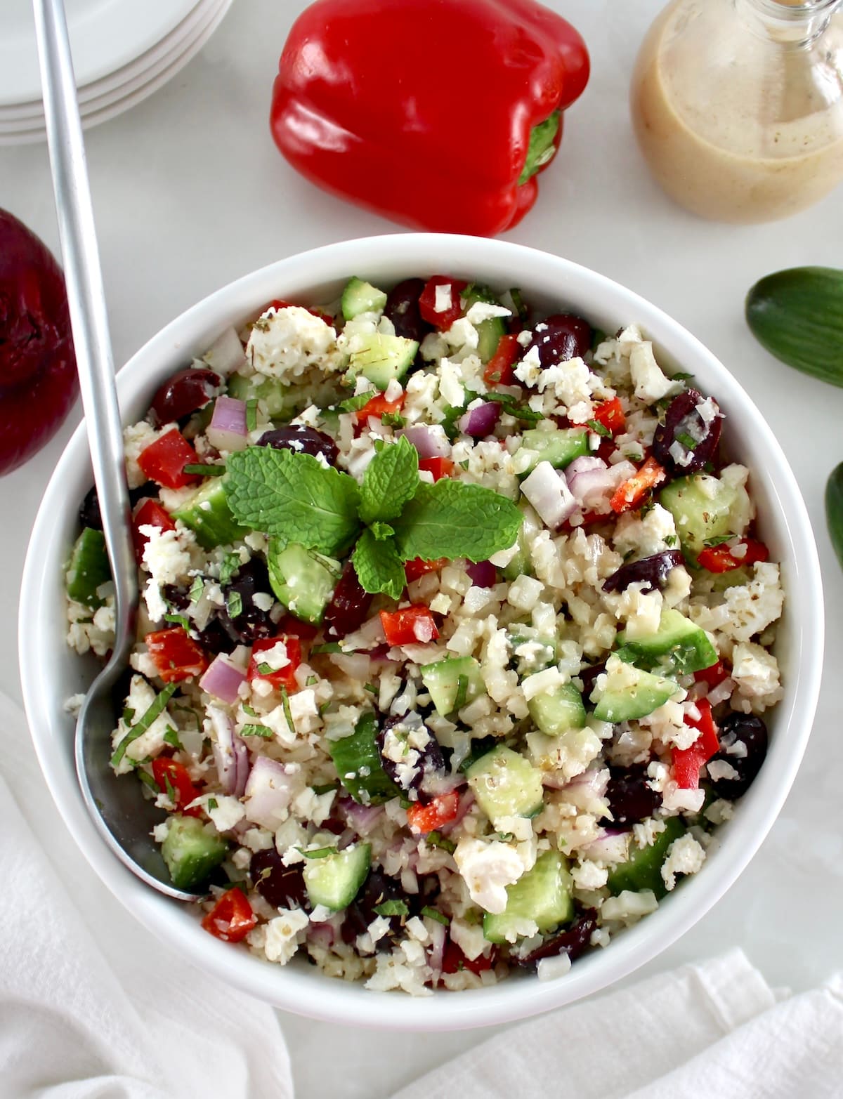 overhead view of Greek Cauliflower Rice in white bowl with silver spoon on side