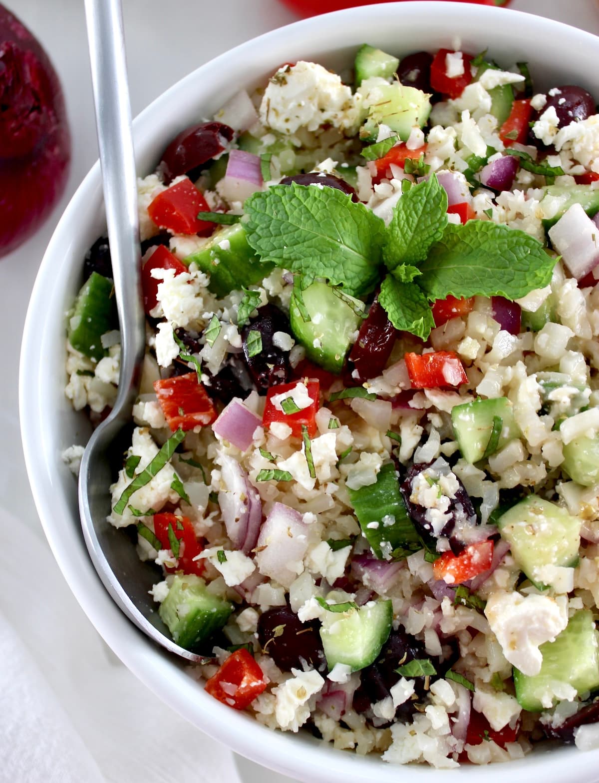 closeup of Greek Cauliflower Rice in white bowl with silver spoon on side