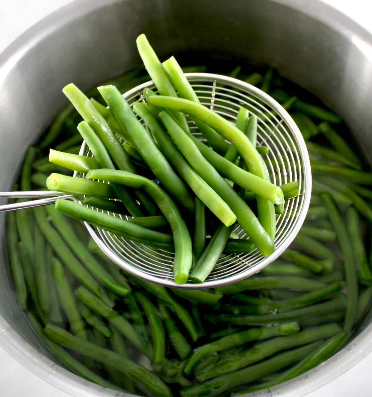 holding up green beans in spider over pot