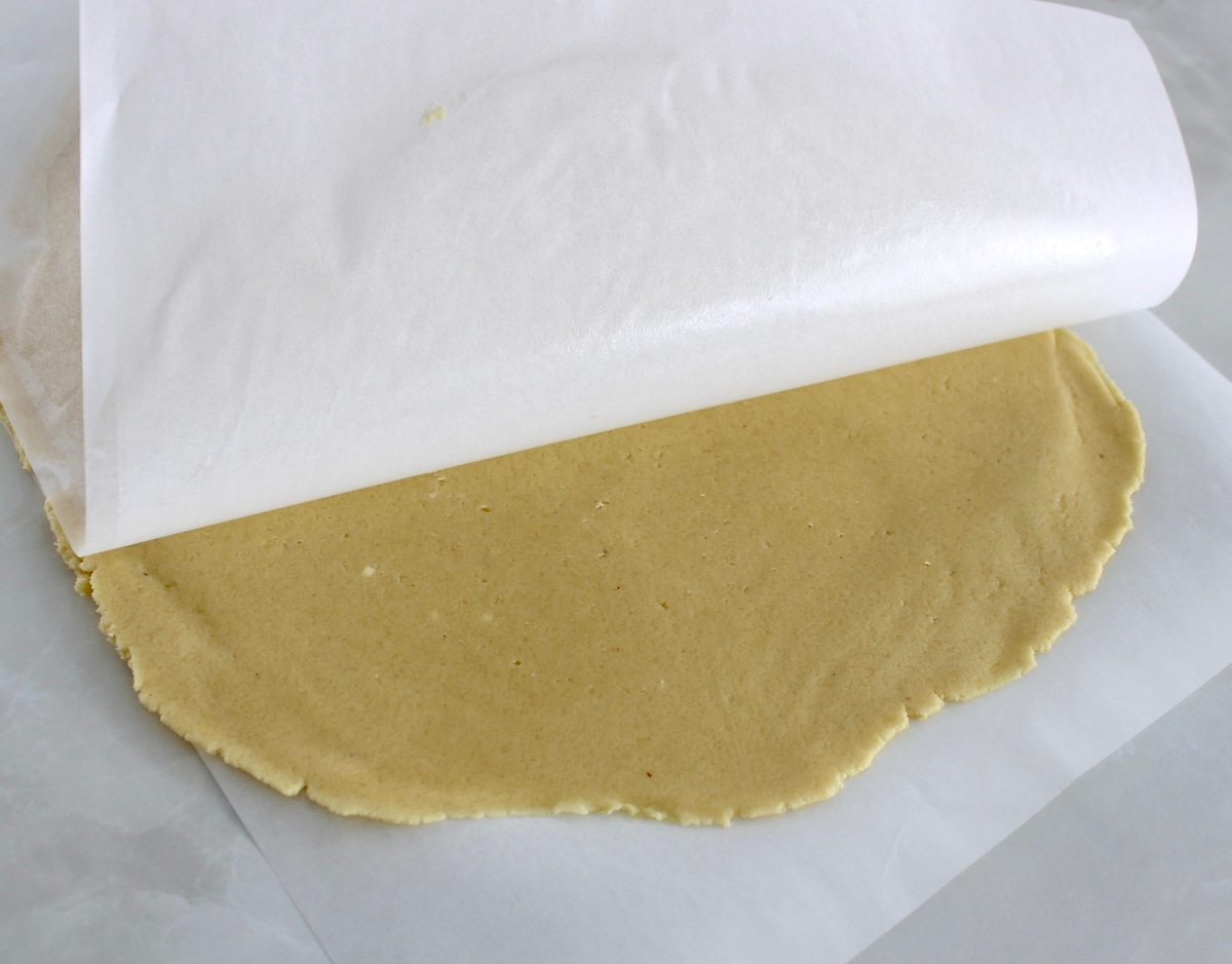 keto pie crust on parchment with parchment on top lifting up