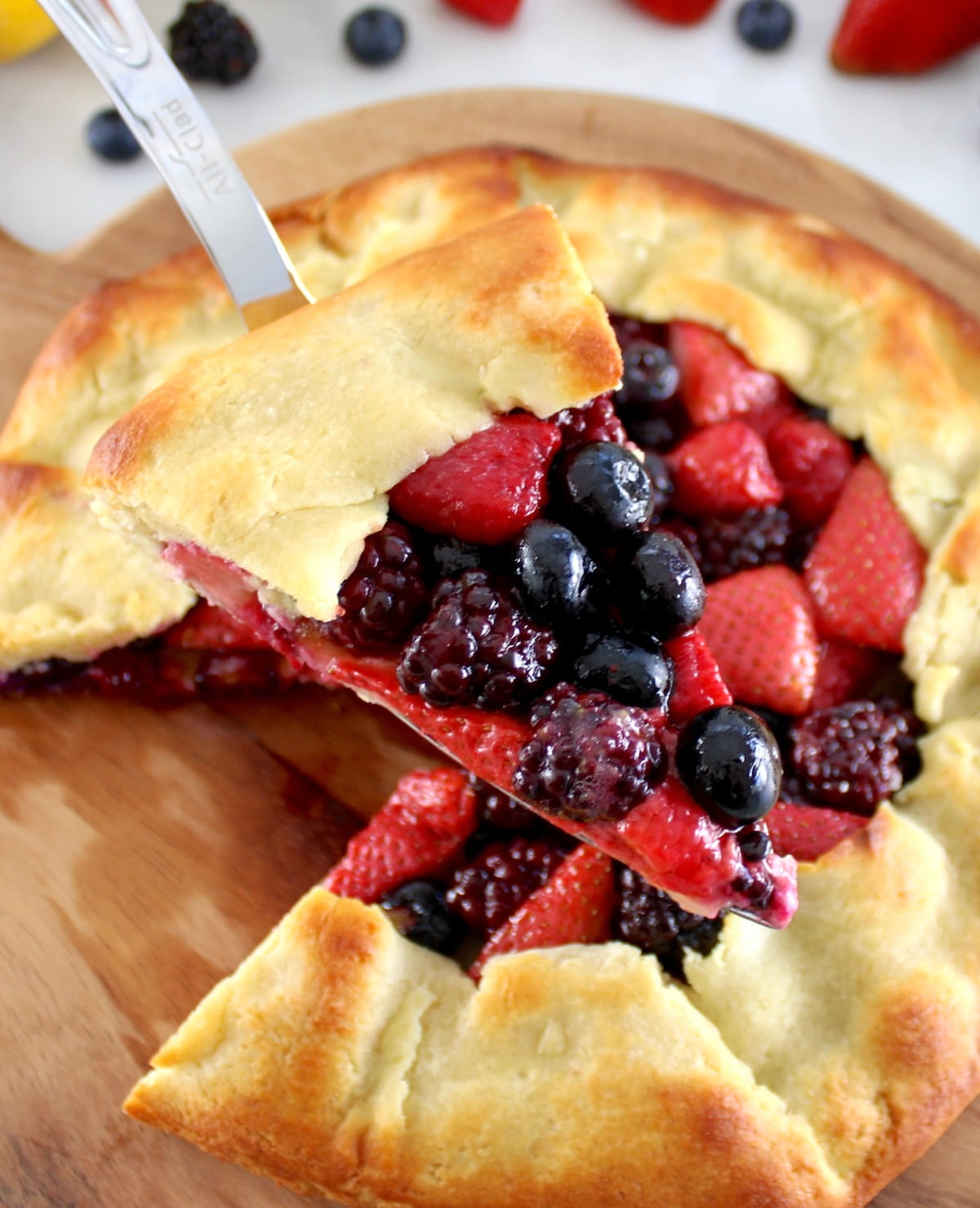 holding up slice of Keto Mixed Berry Galette with silver pie server