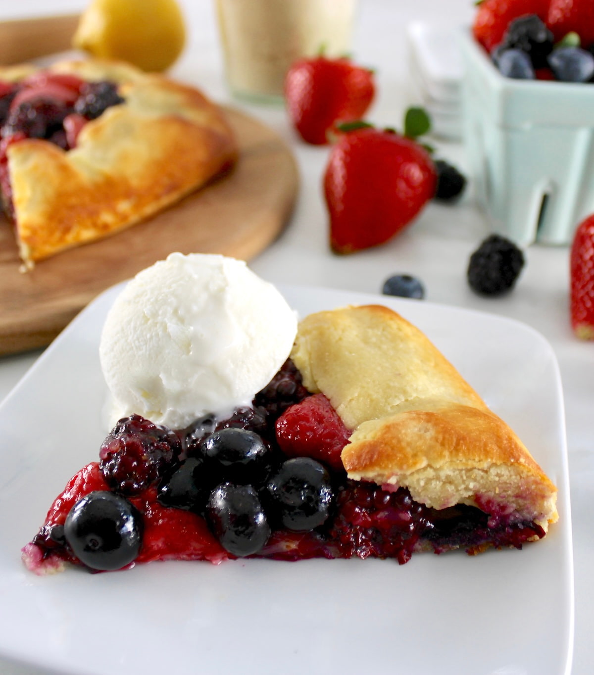 slice of Keto Mixed Berry Galette with vanilla ice cream on side with berries in back