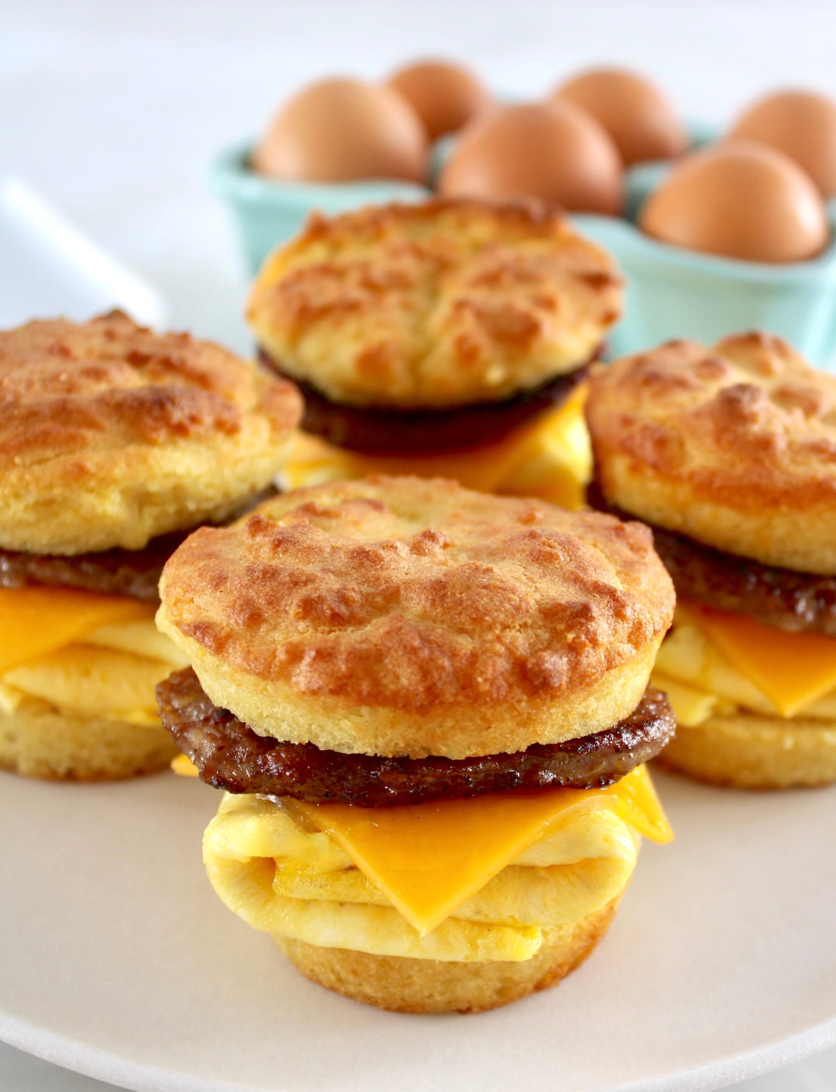 closeup of Keto Sausage Egg and Cheese Biscuits on white plate with eggs in back