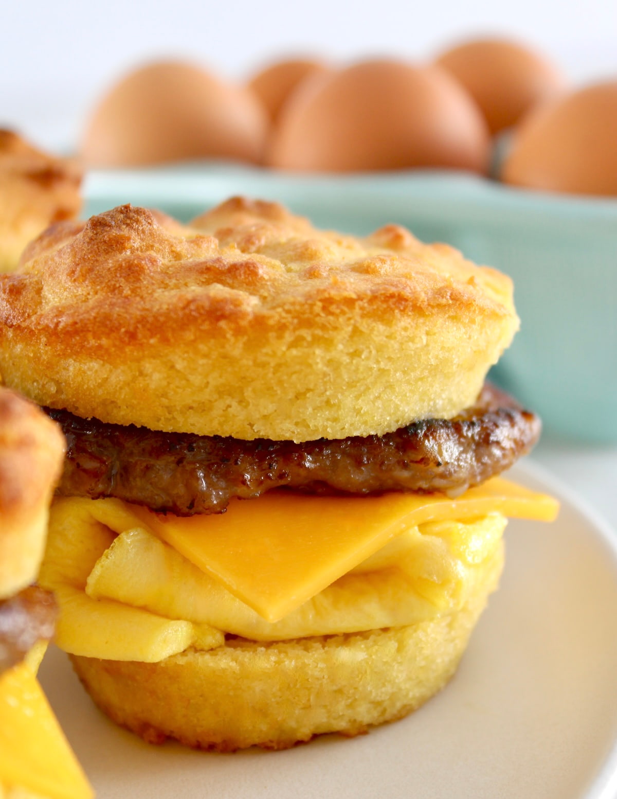 closeup of Keto Sausage Egg and Cheese Biscuits on white plate with eggs in back